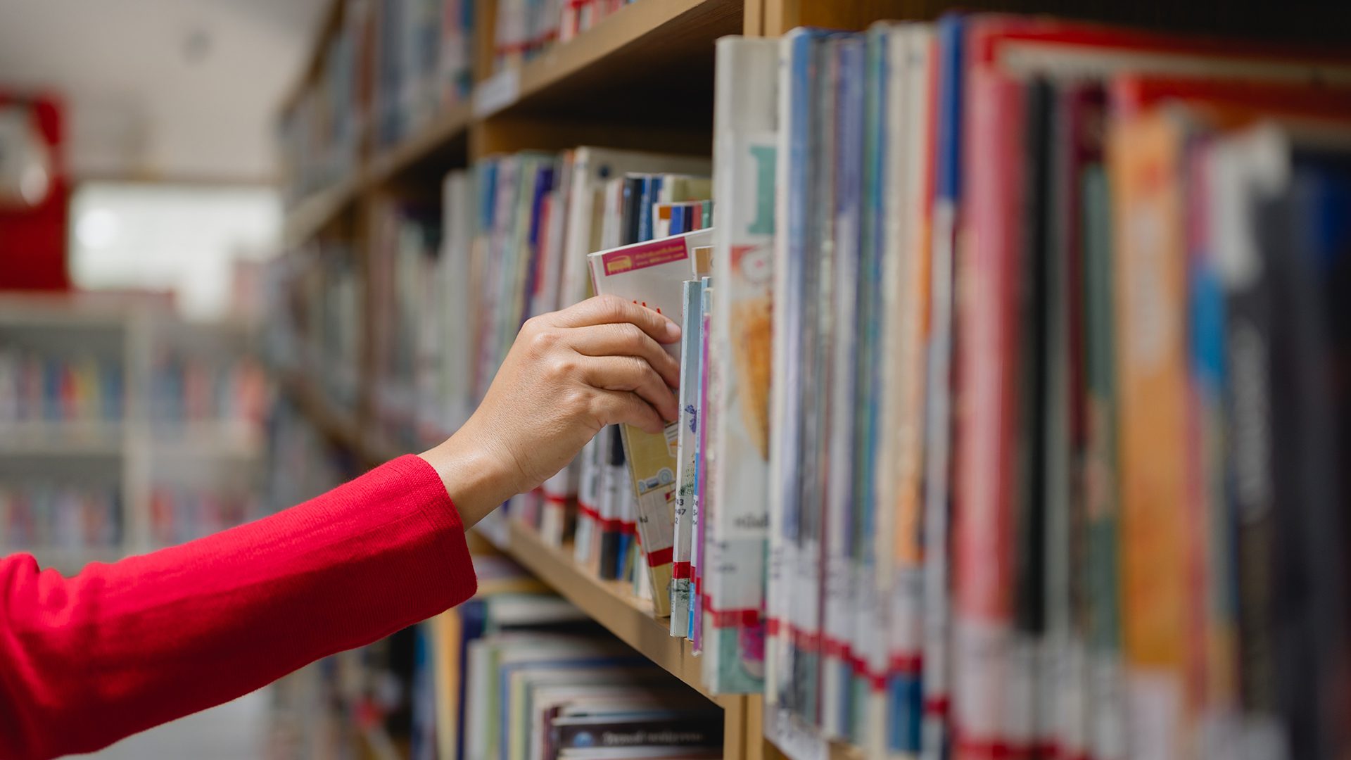 Main prenant un livre sur une étagère dans une bibliothèque.